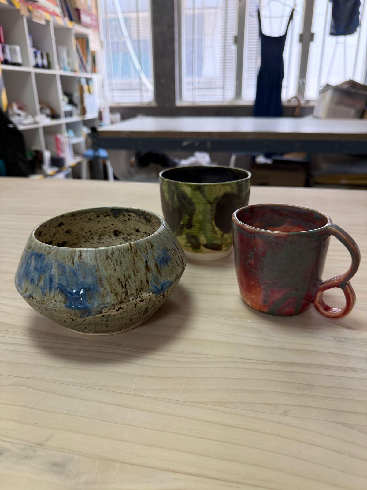 三件手工陶瓷作品：藍霧紋碗、抹茶紋杯、火燒紅釉馬克杯，放喺工作枱上